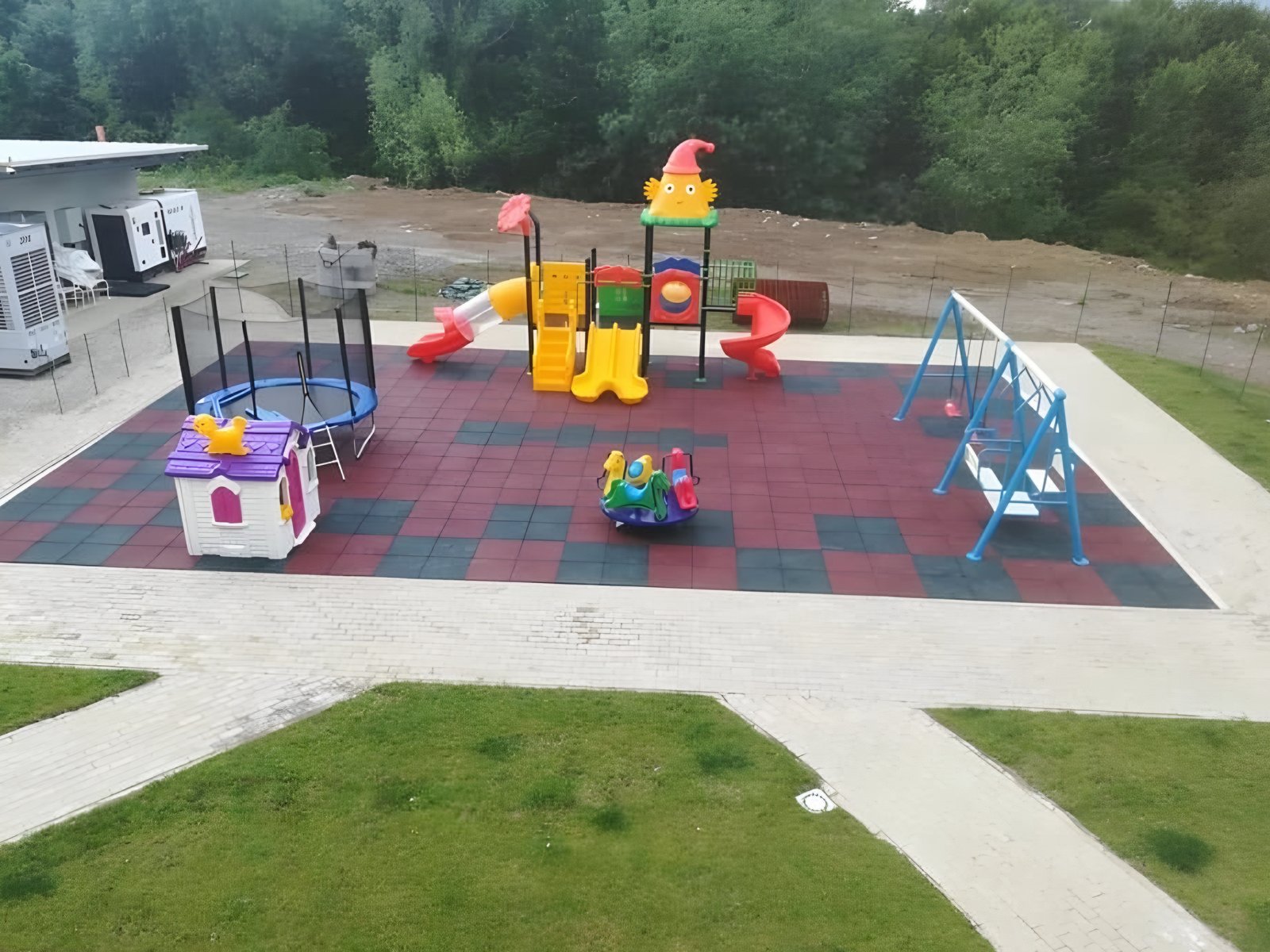 Parcul de joacă văzut de sus: trambulină, căsuță, tobogane, balansoar și leagăne pe pardoseală de cauciuc